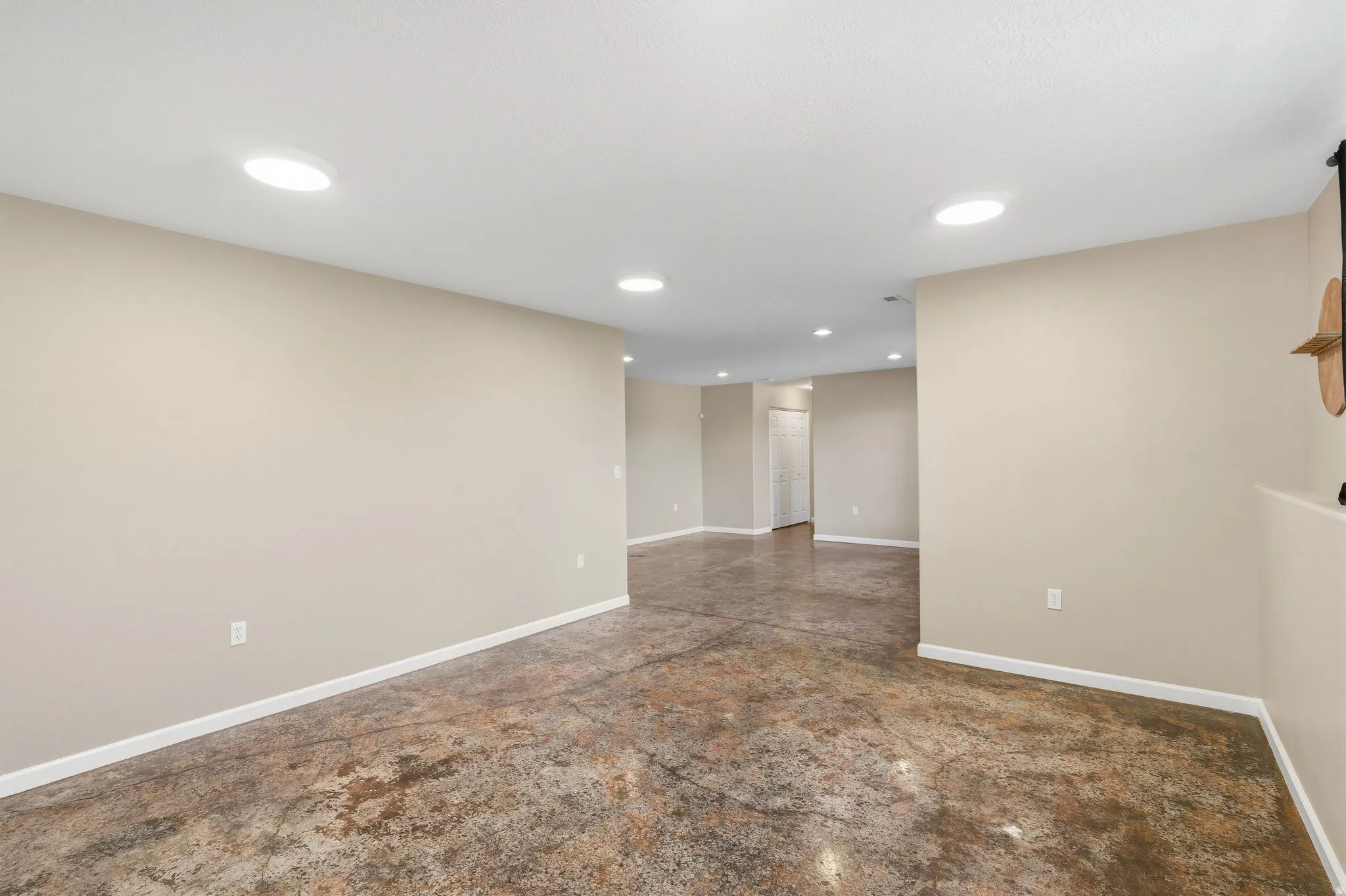 Expansive open-concept room featuring concrete flooring, recessed lighting, and light-toned walls with white baseboards
