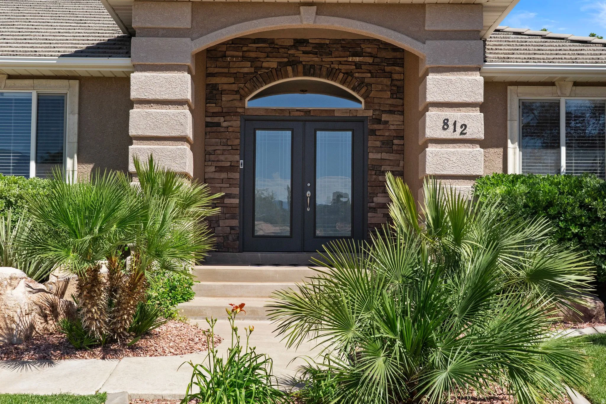 Entryway featuring stone veneer accents, arched transom window, and double glass-paneled doors