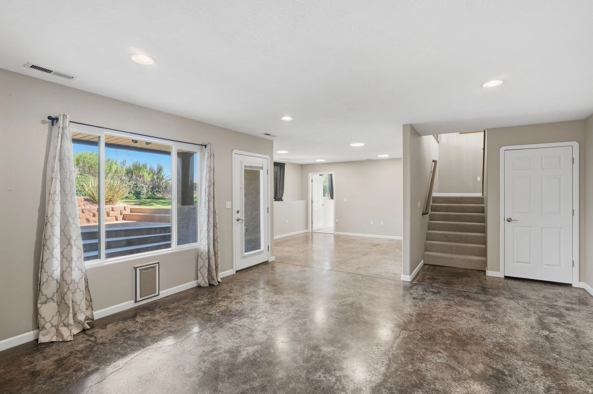 Open-concept living space featuring polished concrete flooring, recessed lighting, and direct outdoor access through a glass-paned door