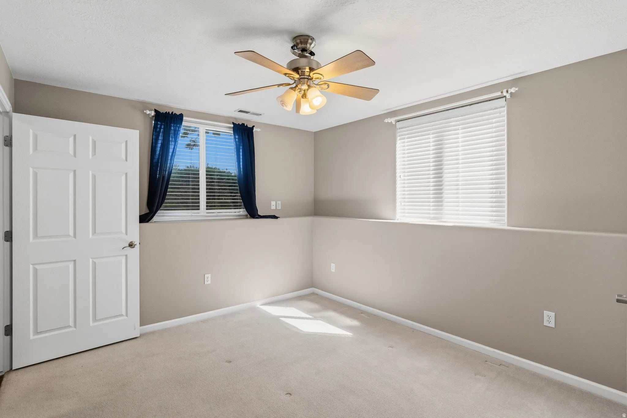 Carpeted interior space featuring a ceiling fan with integrated lighting, a paneled interior door, and two windows with blinds