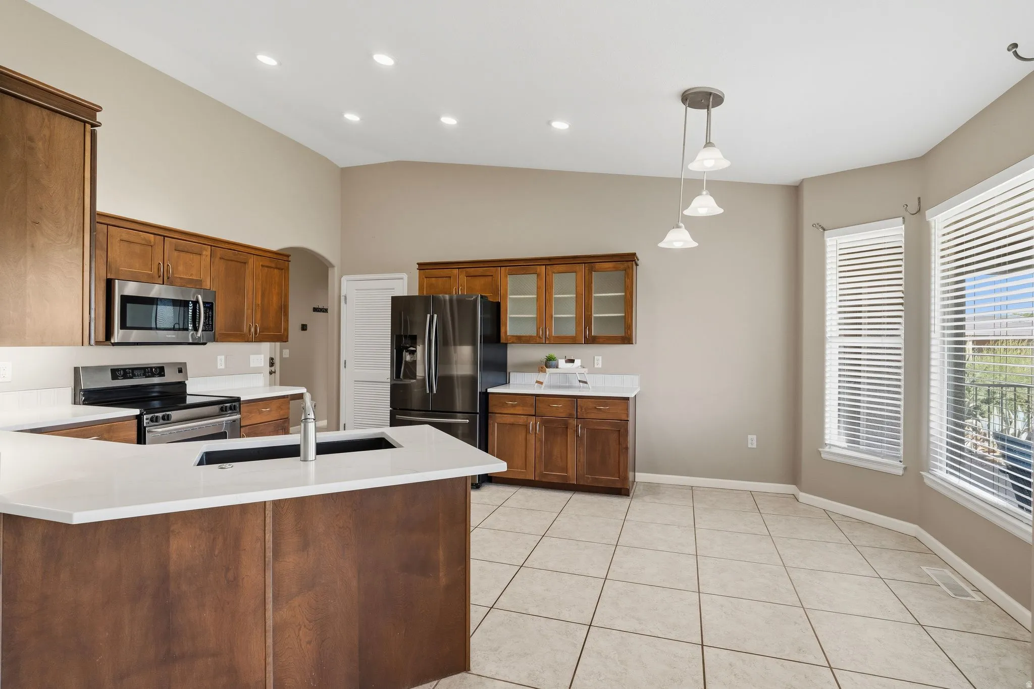 Kitchen featuring a central island with an undermount sink, stainless steel appliances, wood-finish cabinetry, light-toned countertops, and tiled flooring