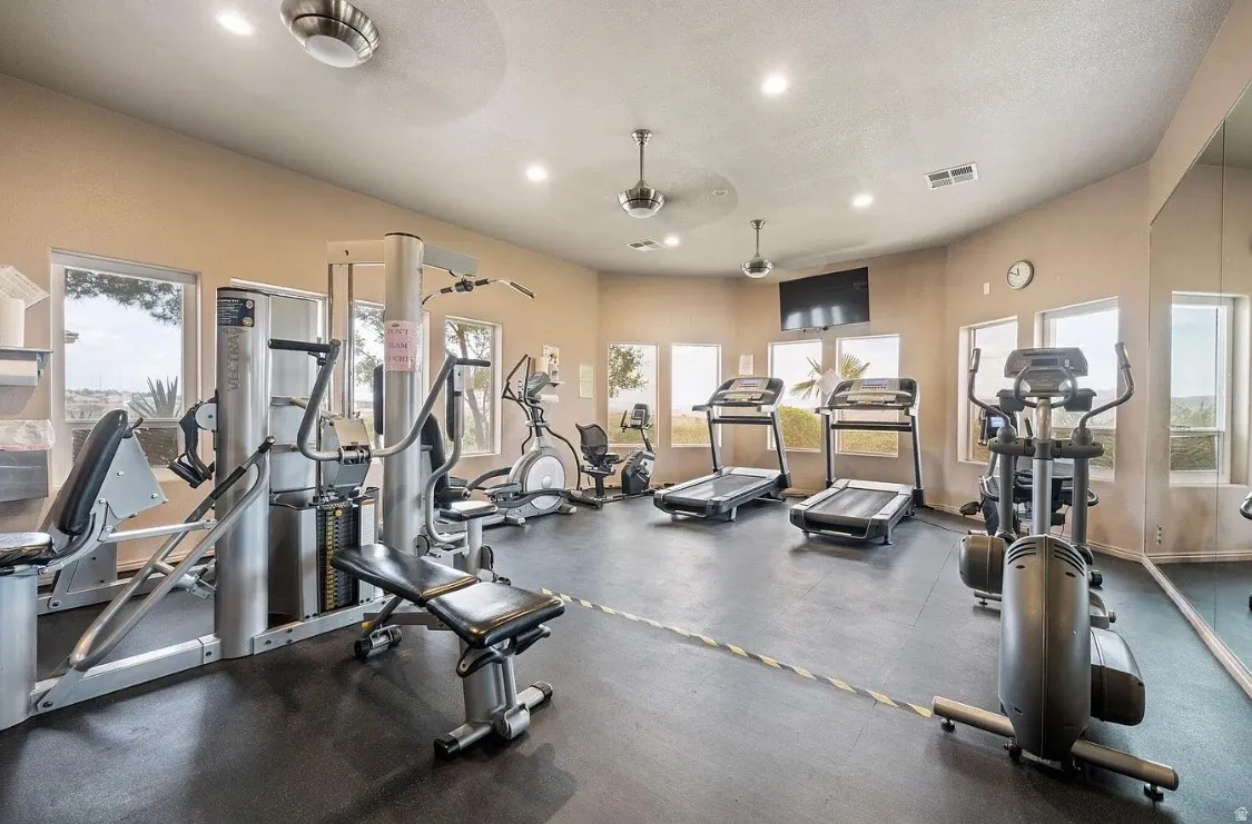 Fitness center featuring extensive exercise equipment, dark rubberized flooring, multiple windows, recessed lighting, and ceiling fans