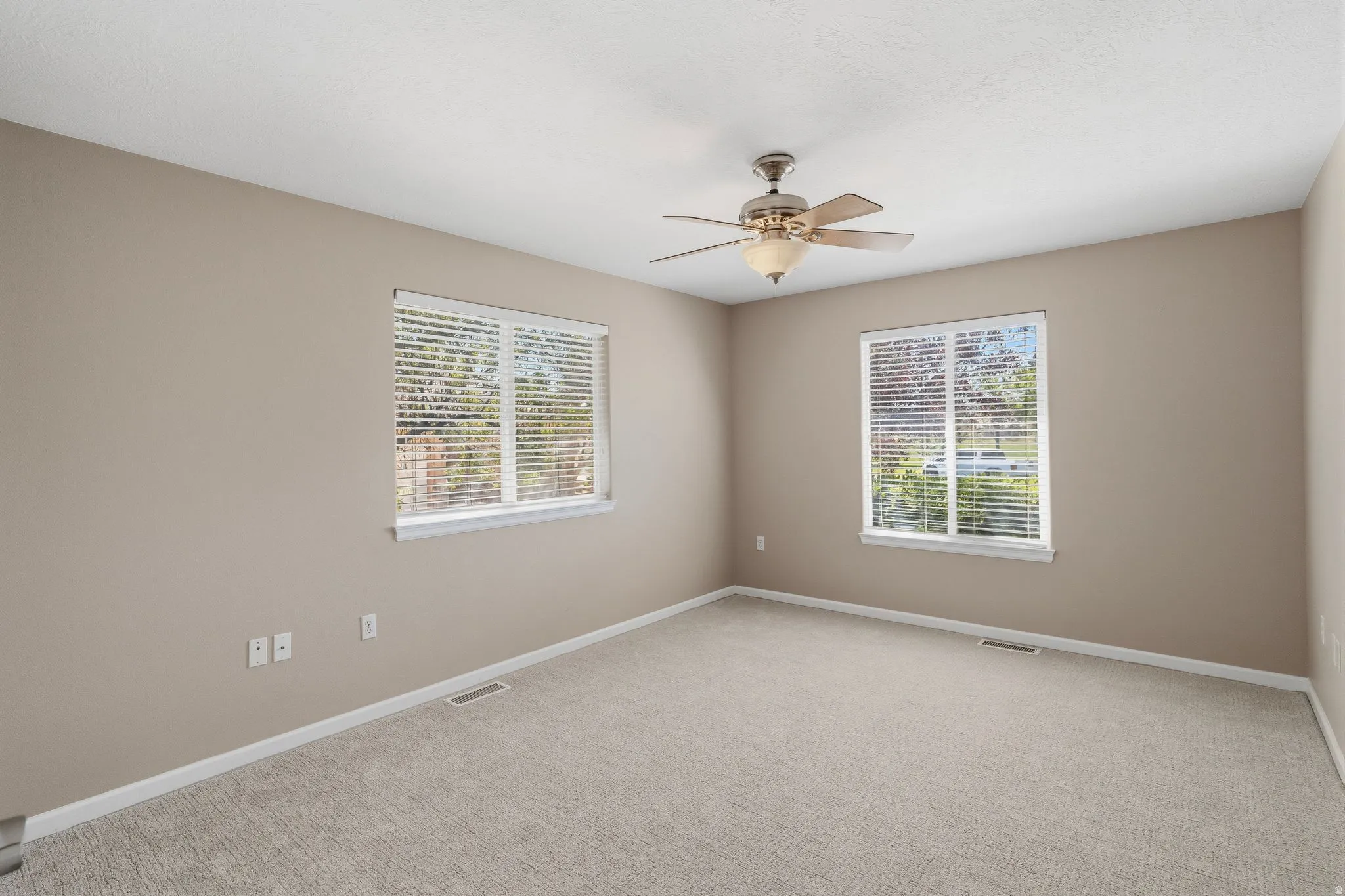Carpeted room with neutral paint, featuring two windows with white blinds, and a ceiling fan with integrated lighting