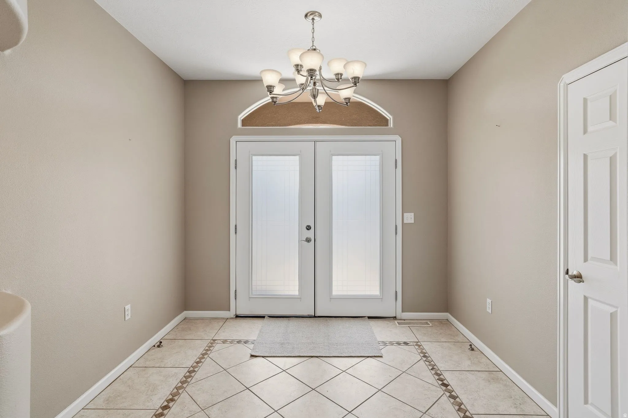 Double entry doors with privacy glass, an arched transom window, and a multi-bulb chandelier