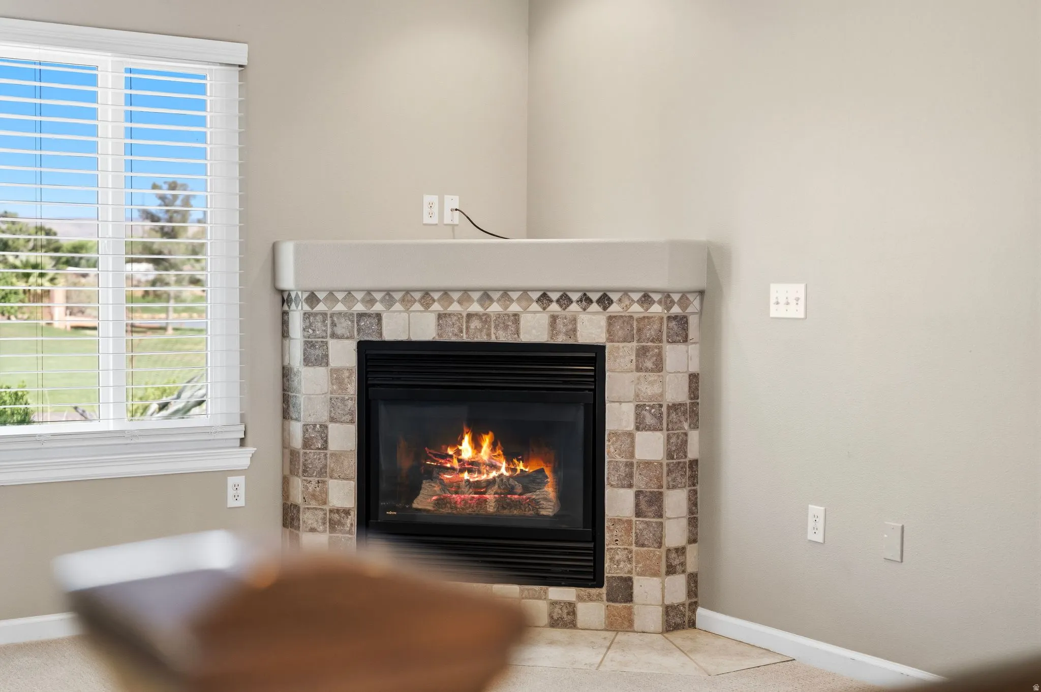 Corner fireplace featuring a patterned tile surround and hearth, with a mantel shelf
