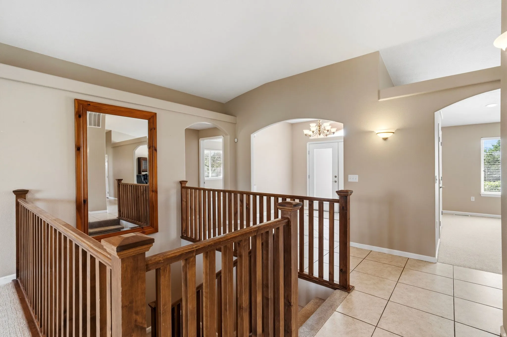Split-level entryway featuring wood railings, neutral wall tones, arched doorways, a built-in wall sconce, and tiled flooring