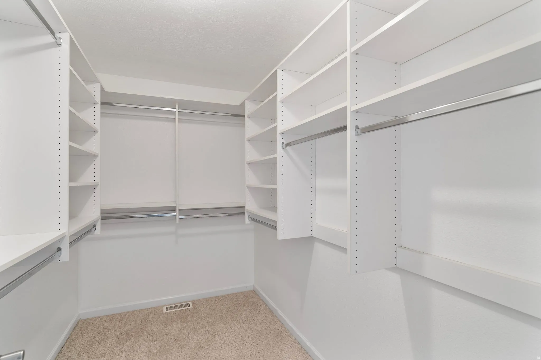 Walk-in closet featuring built-in white shelving, multiple hanging rods, and neutral-toned carpeting