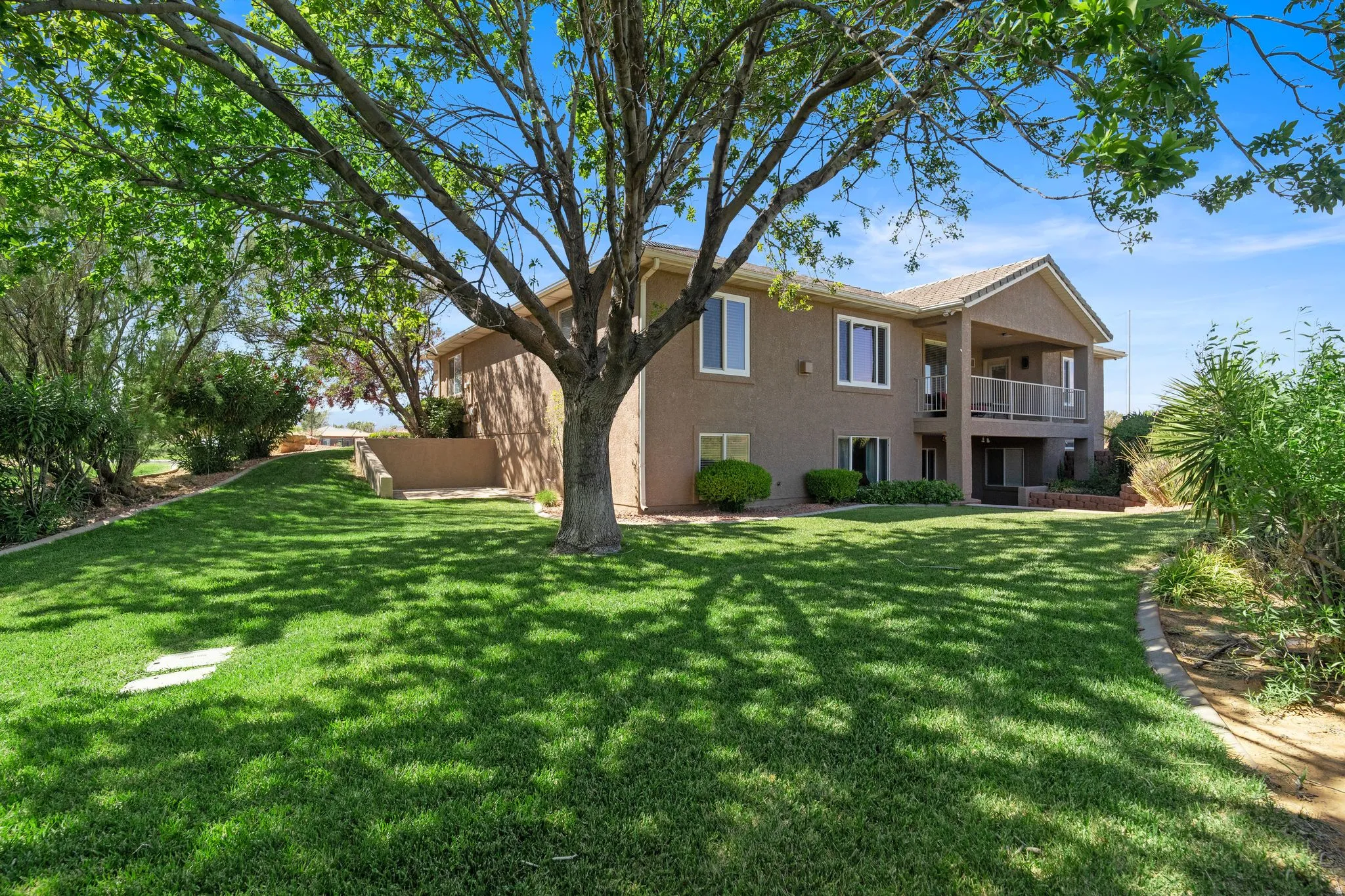 Spacious rear yard featuring extensive green lawn, mature shade trees, a covered patio, and a covered upper-level balcony with metal railing
