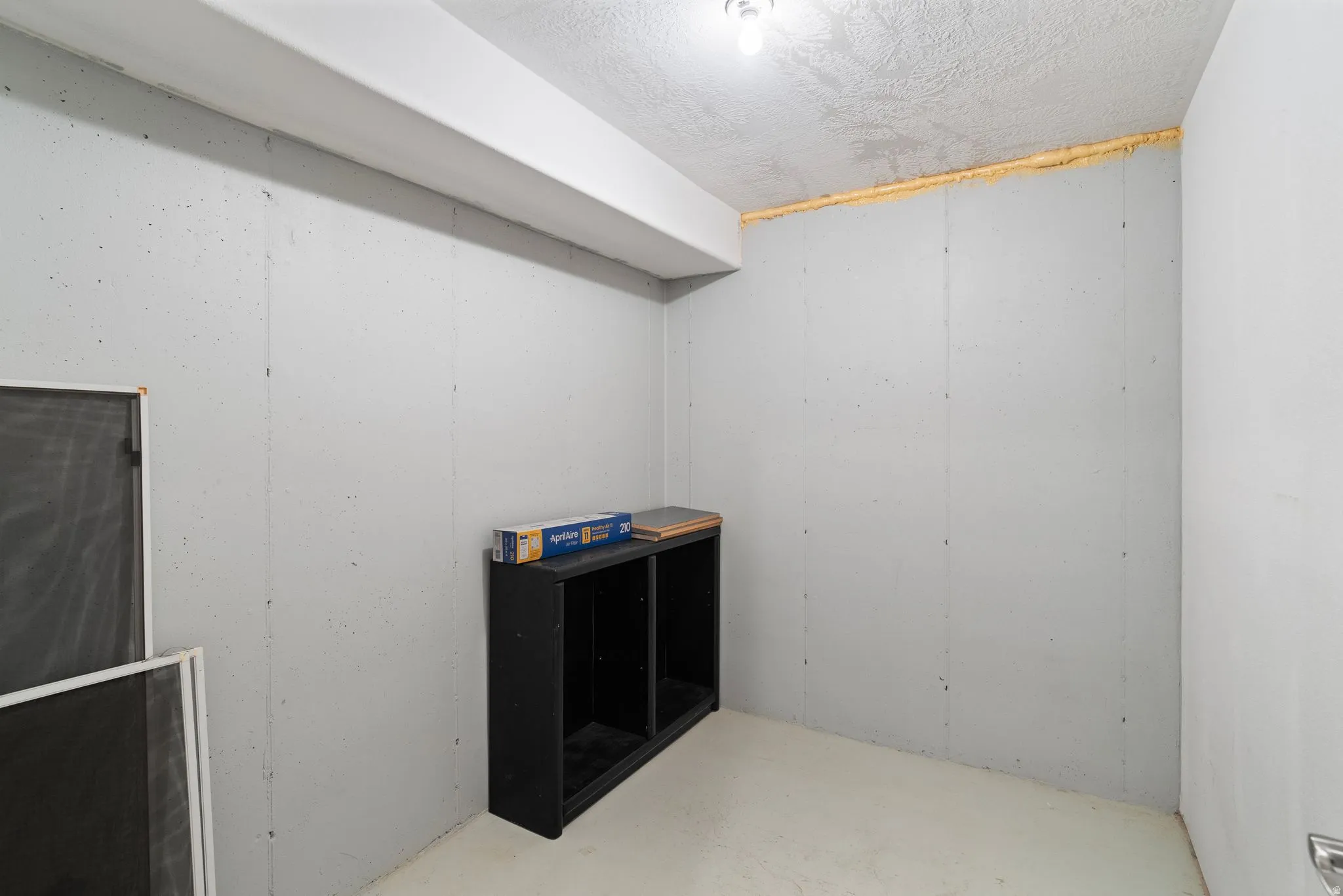 Concrete basement room with a textured ceiling, a visible beam, and a single ceiling light fixture