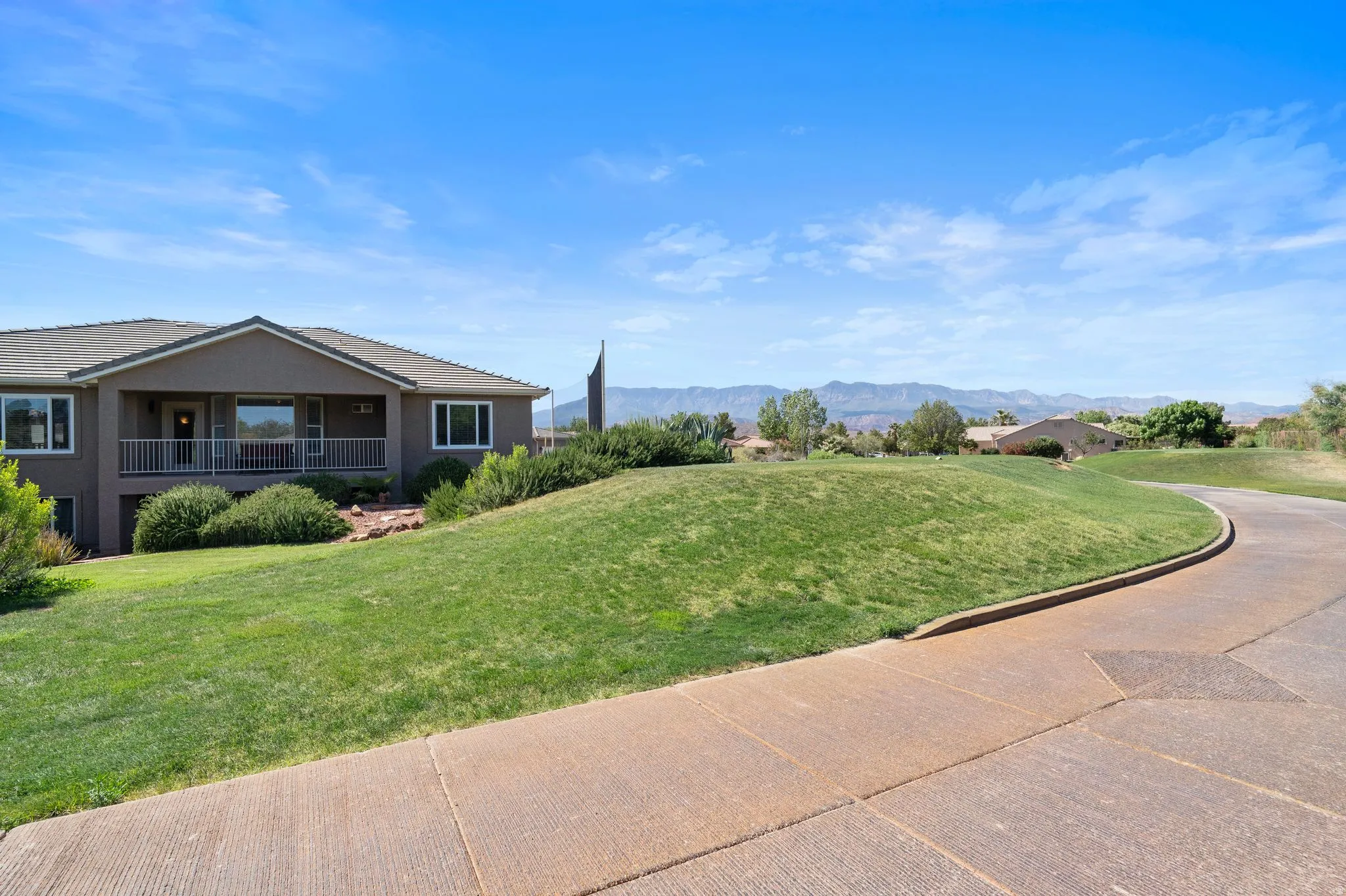 Stucco exterior featuring a covered porch with white railing, mature landscaping, and an expansive lawn