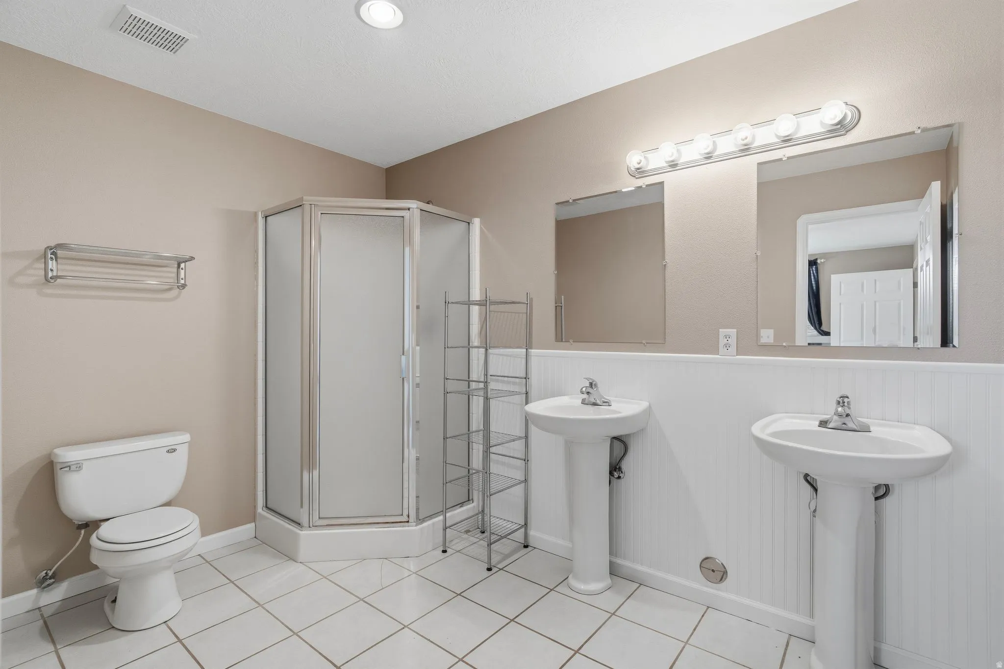 Bathroom featuring a corner shower enclosure, dual pedestal sinks, a toilet, and white tile flooring