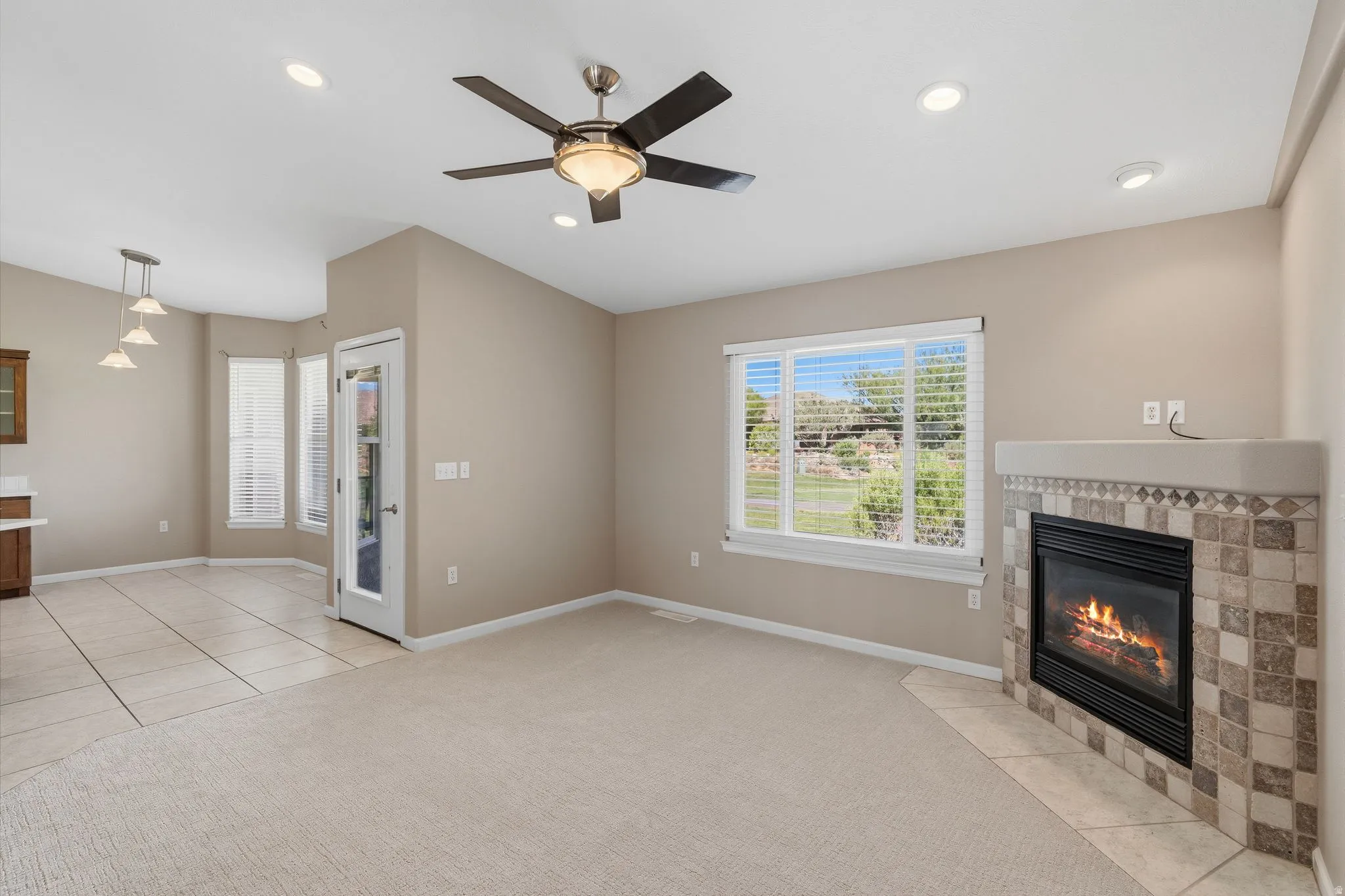 Living area featuring a gas fireplace with a tiled surround and hearth, neutral carpeting, and a ceiling fan with integrated lighting