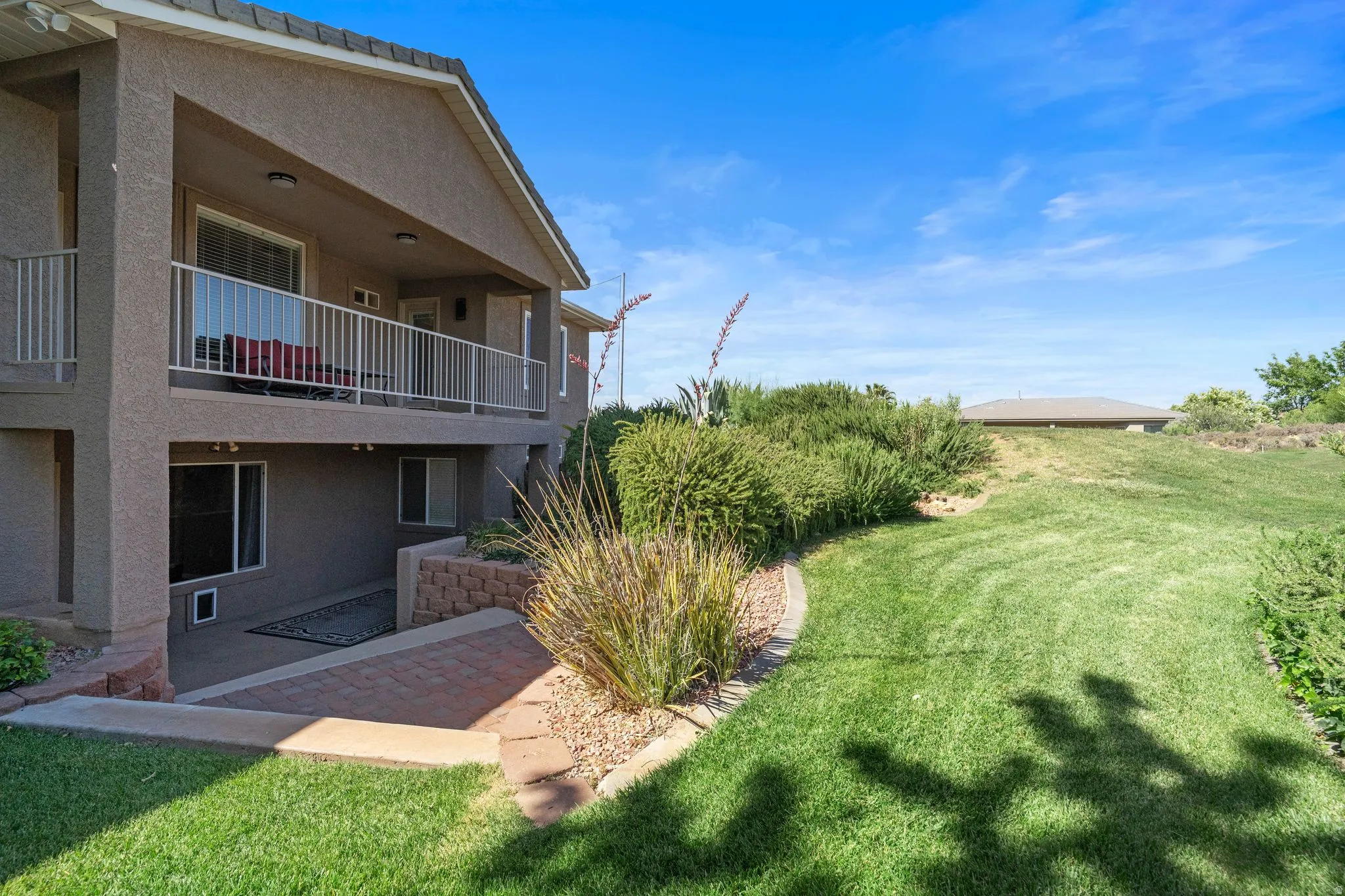 Two-story stucco exterior featuring an upper balcony, a lower covered patio, and a sloped lawn