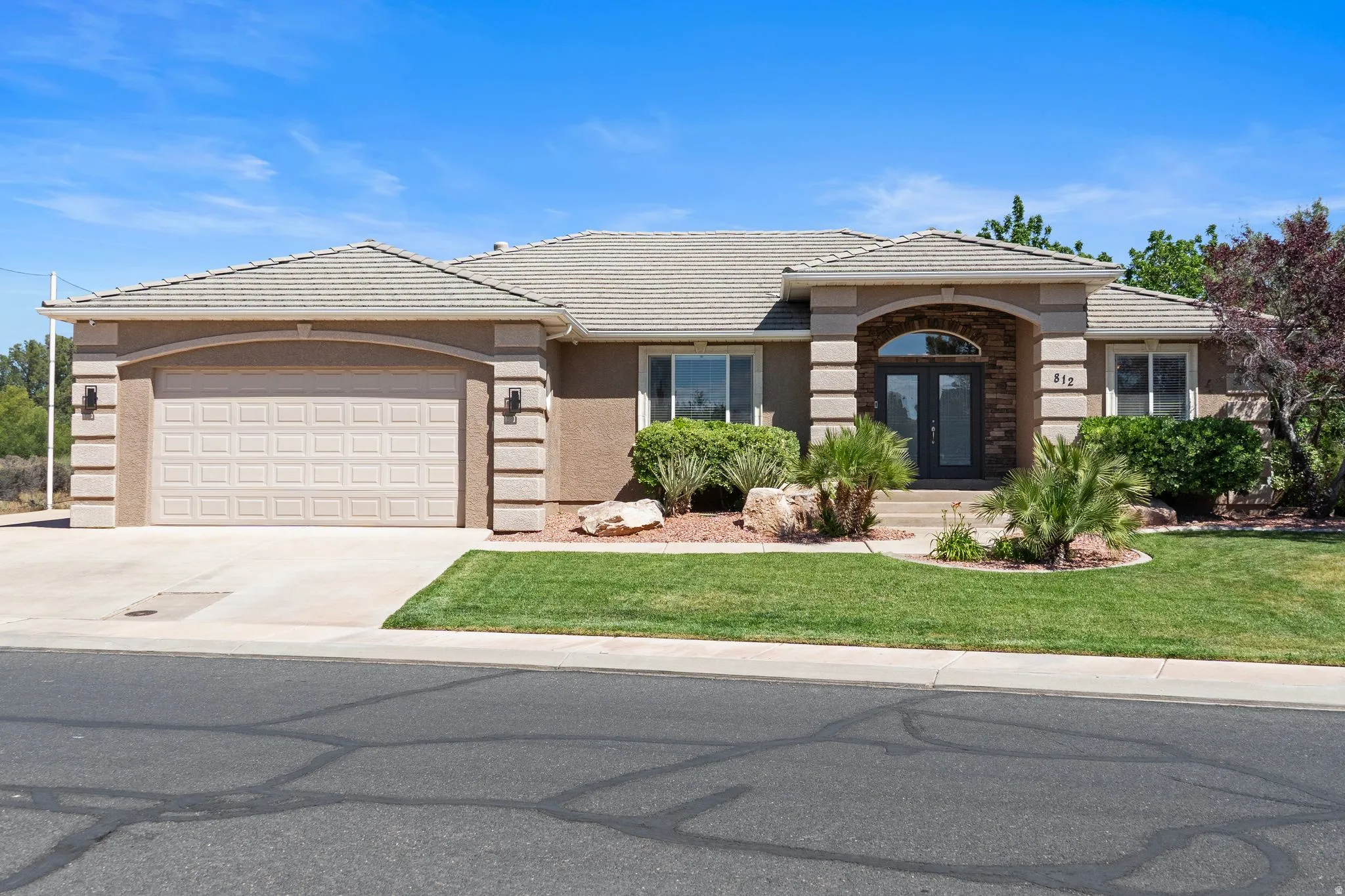 Single-story residence featuring a tile roof, an arched entry with stone accents, a two-car garage, and a manicured front lawn with mature landscaping