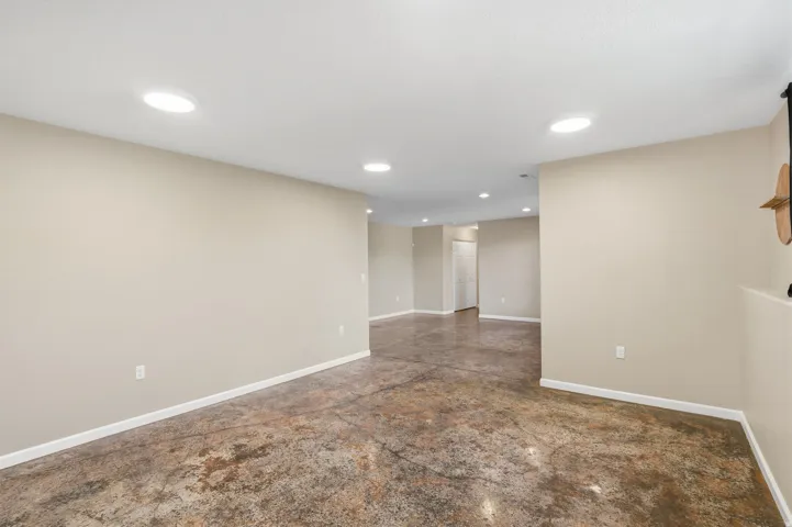 Expansive open-concept room featuring concrete flooring, recessed lighting, and light-toned walls with white baseboards