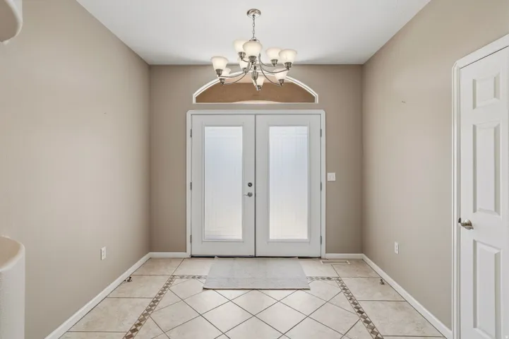 Double entry doors with privacy glass, an arched transom window, and a multi-bulb chandelier