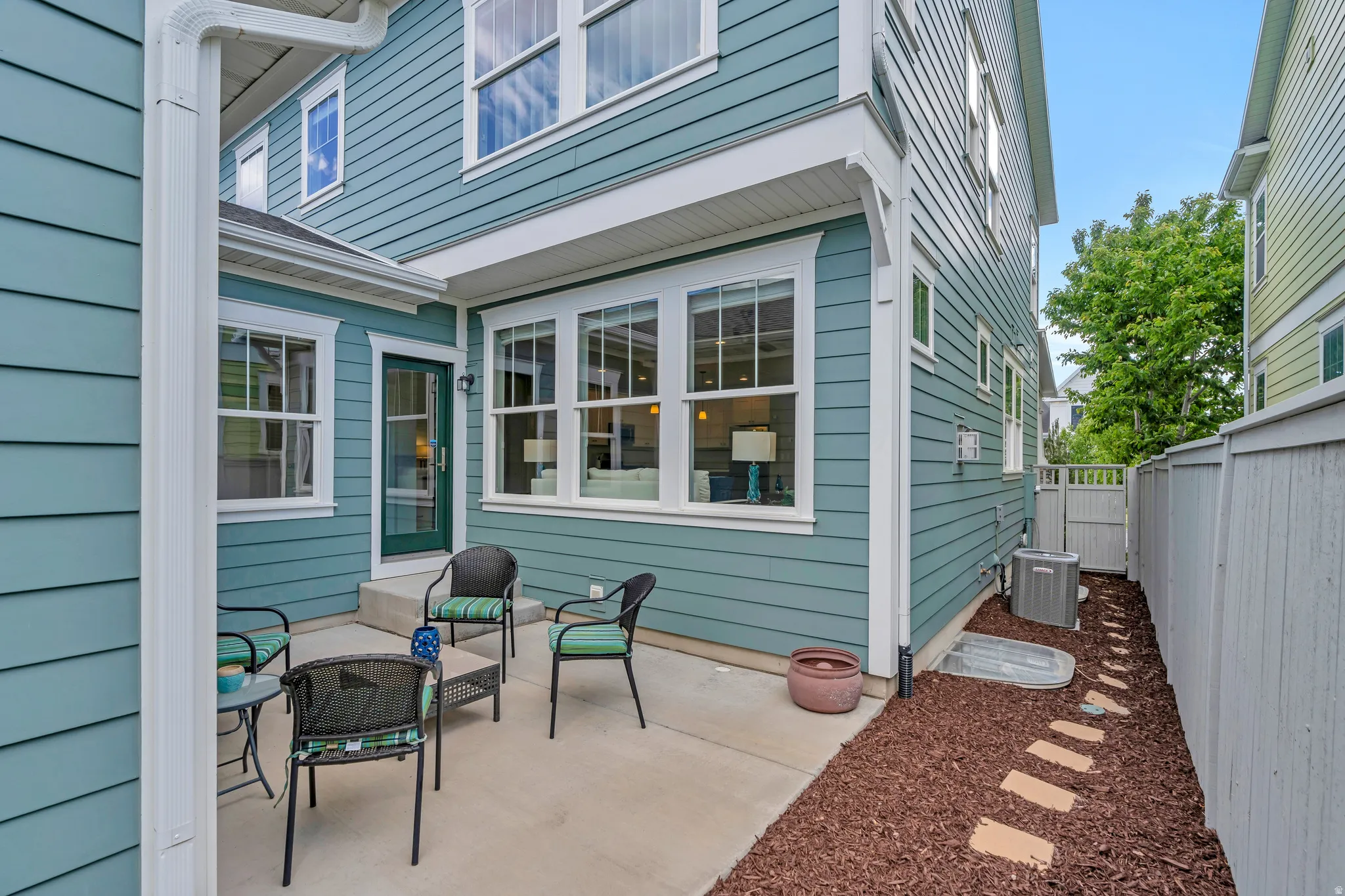 Exterior patio area featuring concrete flooring, a teal-colored siding facade, white trim, and a fenced perimeter