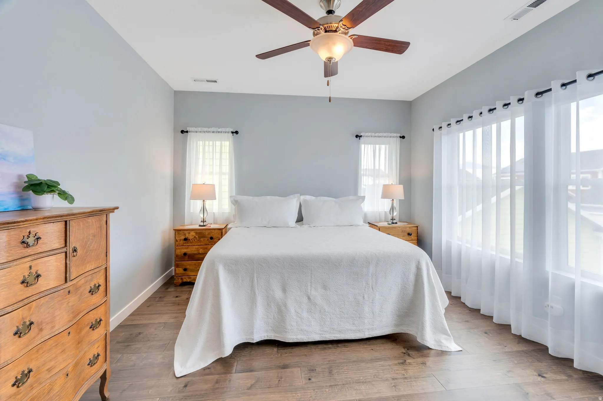 Spacious room featuring wood-finish flooring, light grey walls, and a ceiling fan with integrated lighting