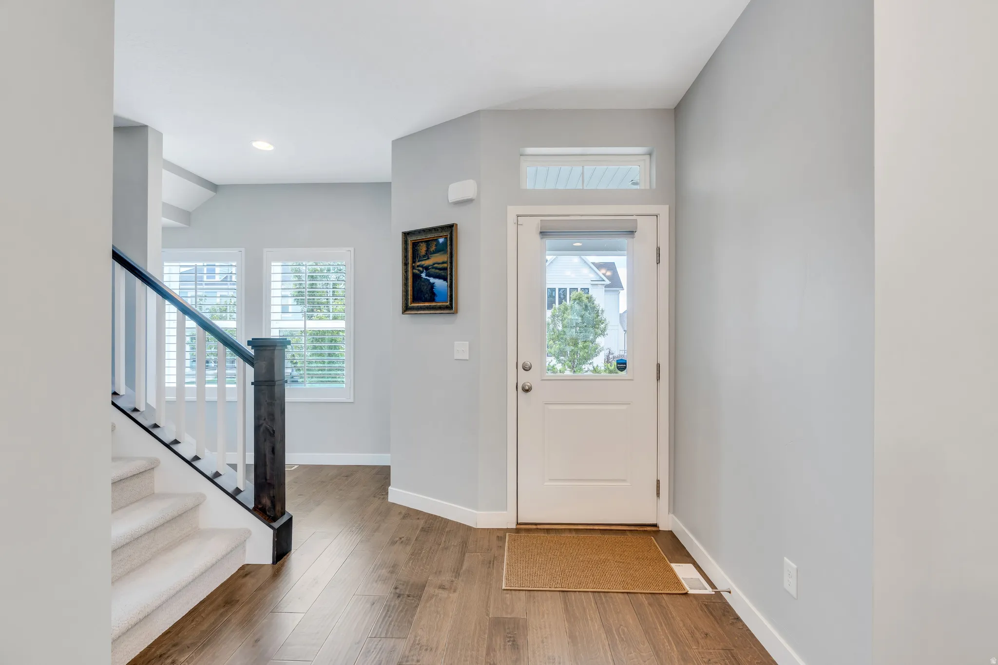 Entryway featuring wood-finish flooring, a staircase with white risers and carpeting, and a white front door with a transom window