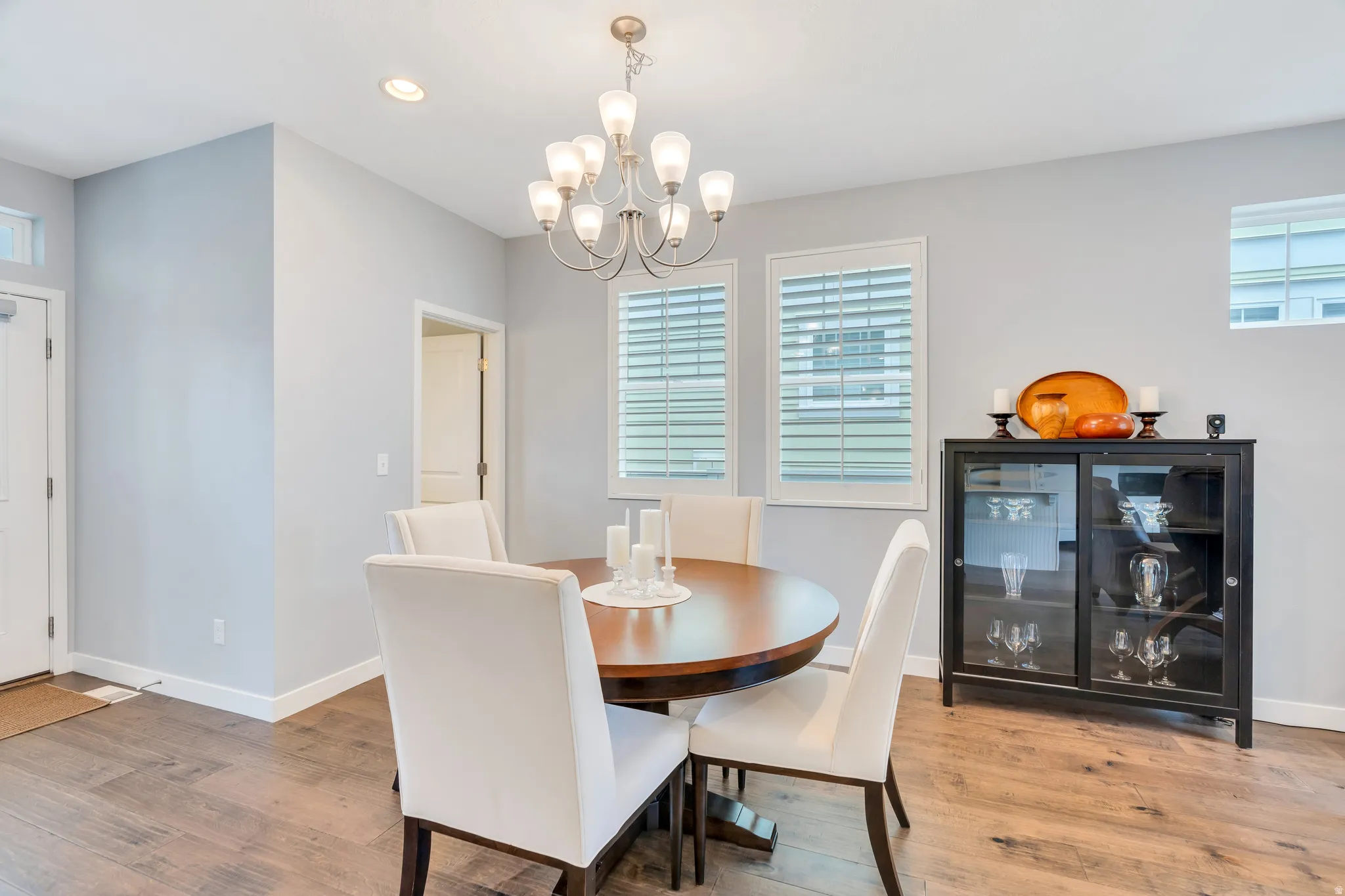 Dining area featuring wood-finish flooring, two large windows with plantation shutters, a multi-light chandelier, and recessed lighting