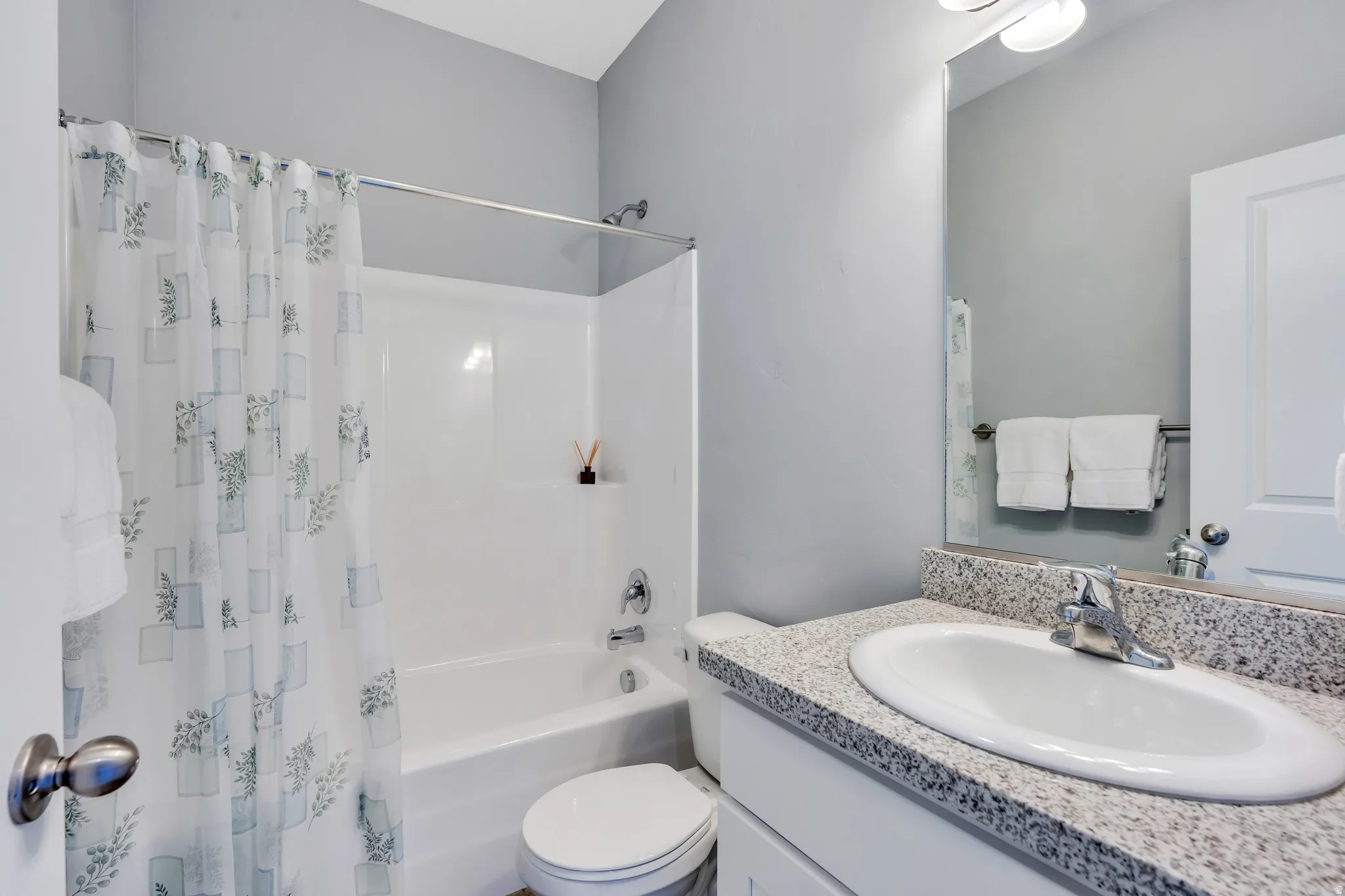 Bathroom featuring a white bathtub and shower combination with chrome fixtures, a white toilet, and a vanity with a white basin sink and a speckled countertop