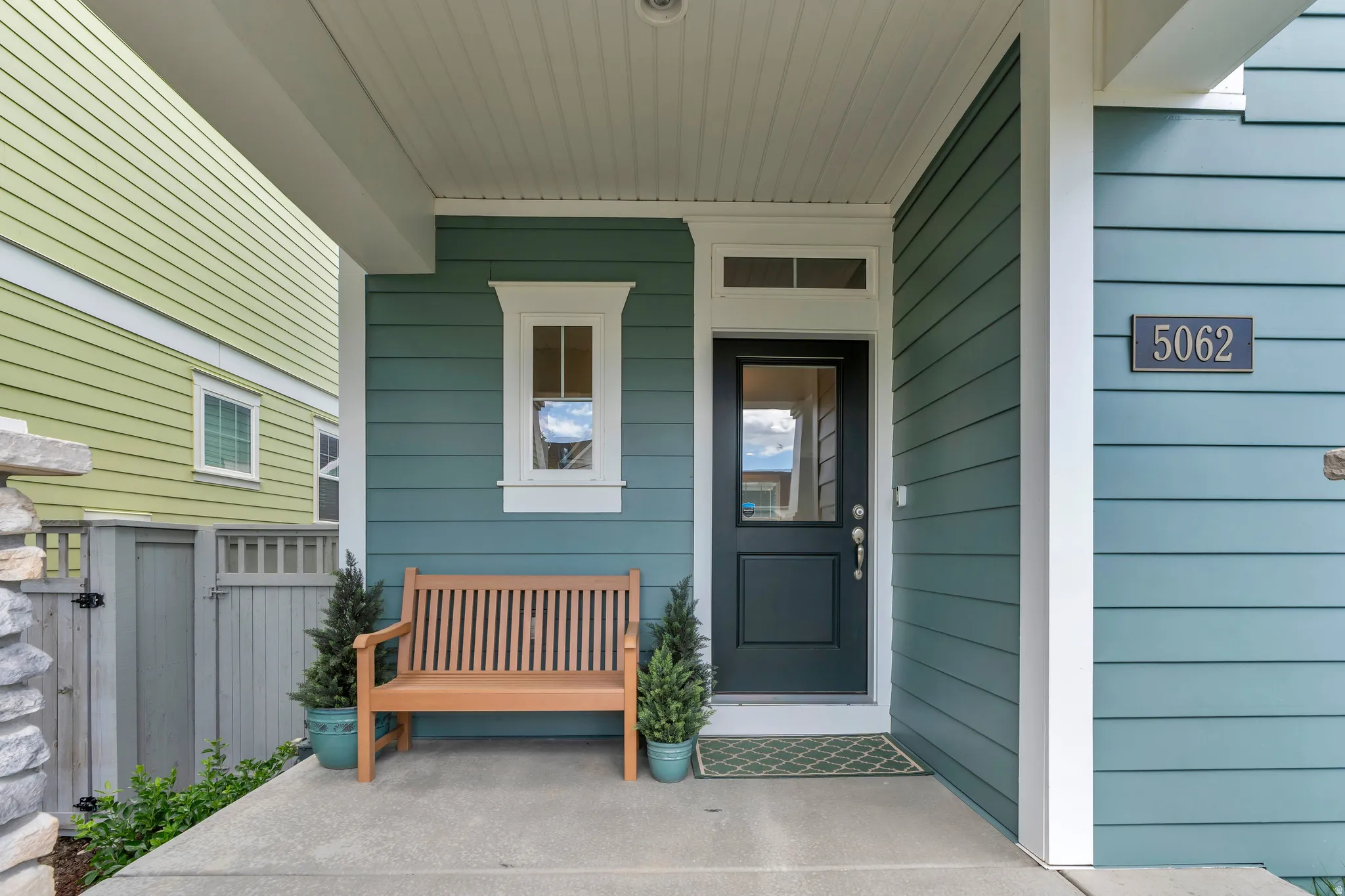 Covered entry with concrete patio, featuring a dark panel door with transom window, horizontal siding, and decorative window trim