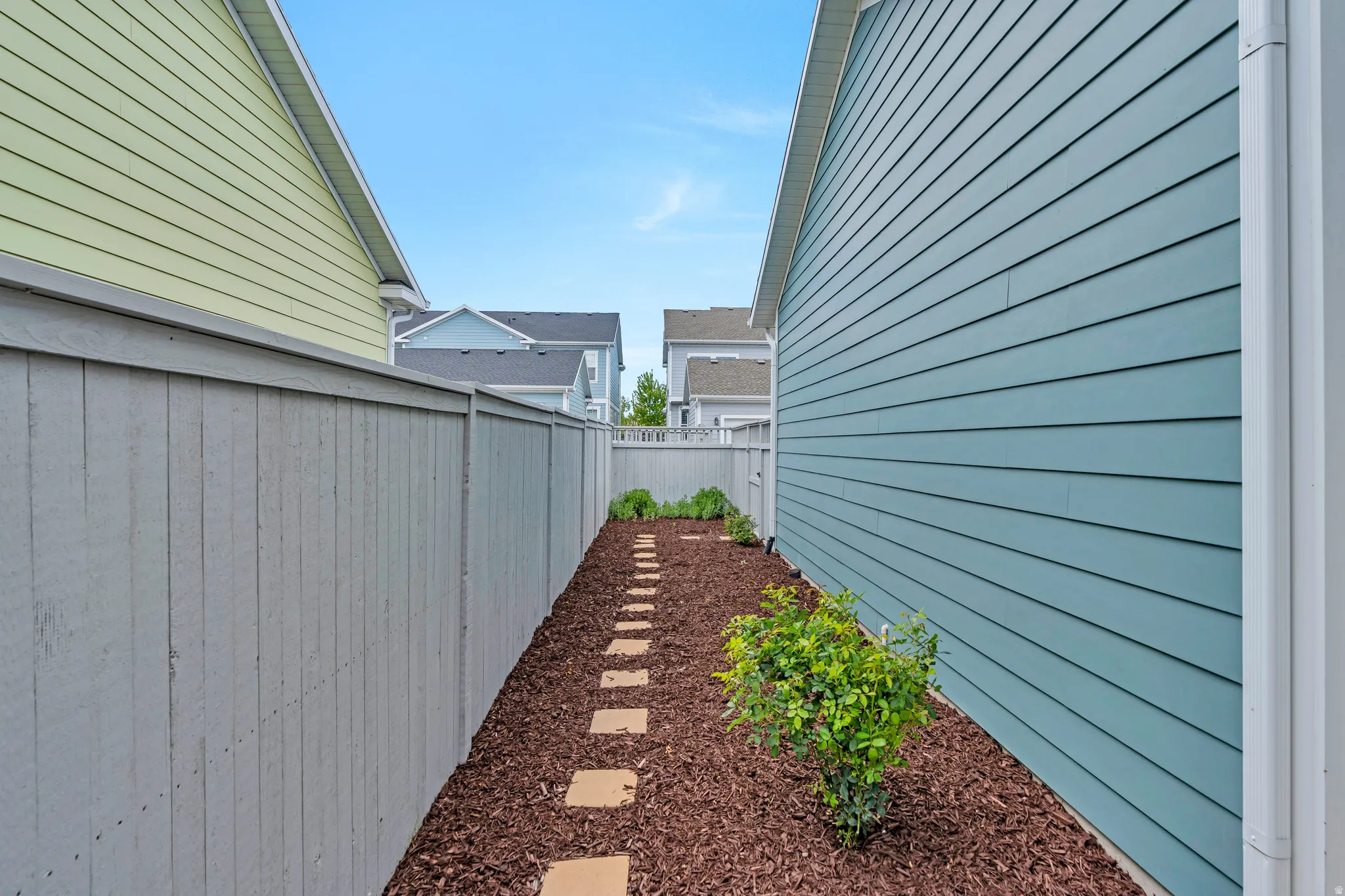 Side yard featuring a stone paver pathway, wood chip ground cover, and planted shrubs