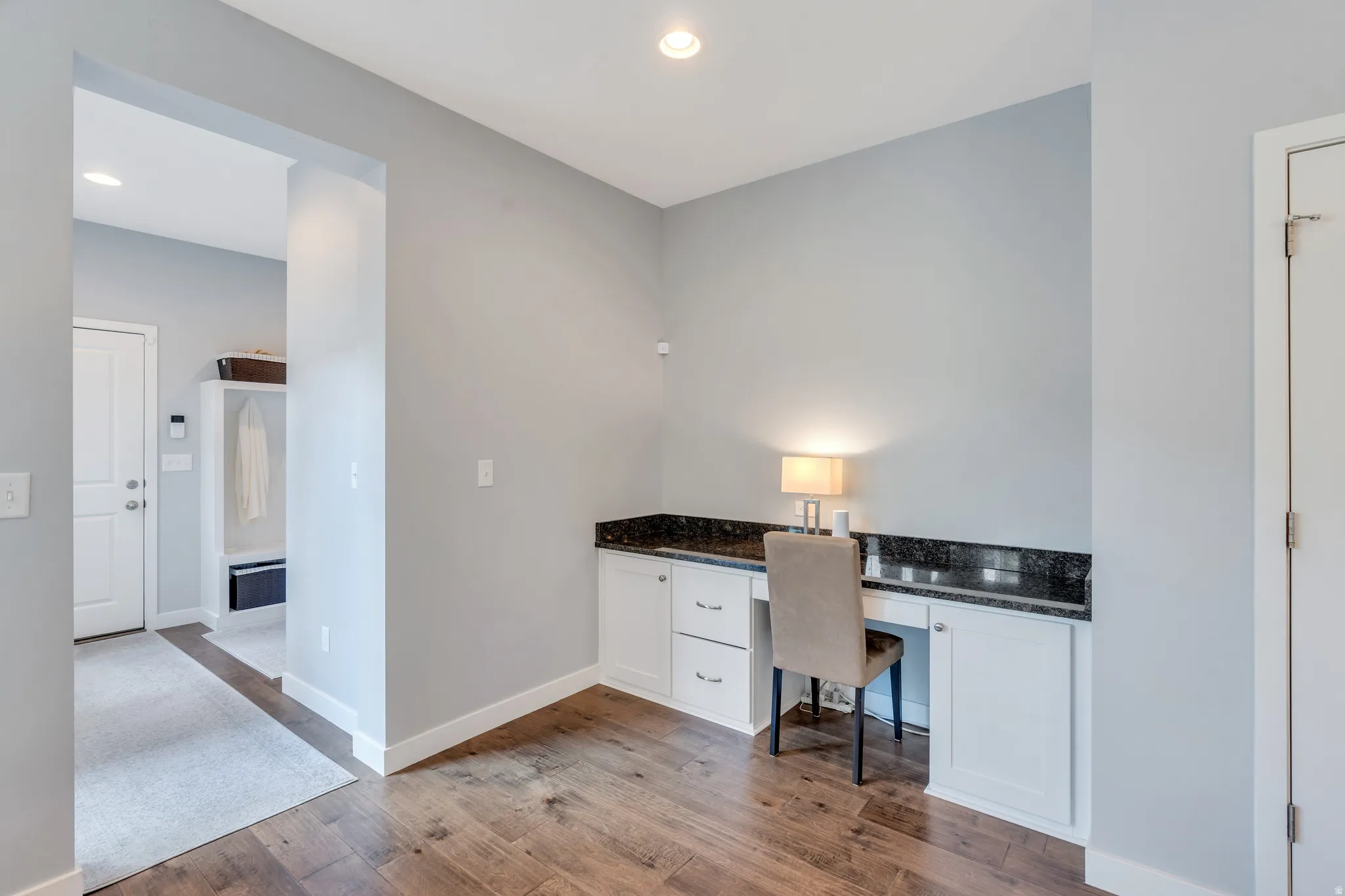 Built-in desk area featuring white cabinetry, dark stone countertop, and wood-finish flooring