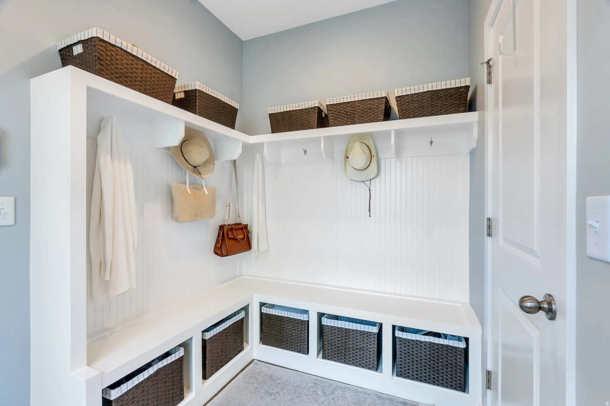 Built-in mudroom bench with cubby storage, beadboard paneling, upper shelving, and coat hooks