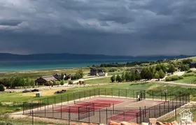 Outdoor multi-sport court featuring tennis court lines and a basketball hoop, enclosed by a black metal fence