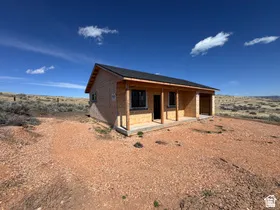 Single-story structure with a dark shingle roof, unfinished exterior siding, and a covered porch supported by wood posts