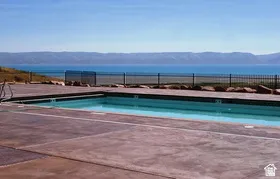 Swimming pool with concrete surround and black metal fencing overlooking a large body of water and distant mountains