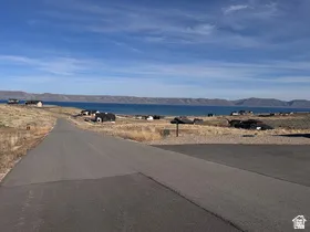 Paved road offering access to a body of water with distant mountains under a blue sky