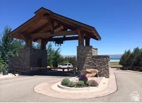 Stone pillar entry gate featuring a substantial timber frame overhead structure, integrated landscaping with decorative rocks and plantings, and paved roadway surfaces