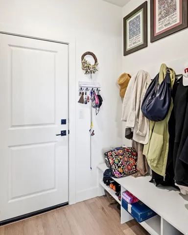 White paneled door with matte black hardware, light wood-finish flooring, and a built-in white storage bench with integrated shelving