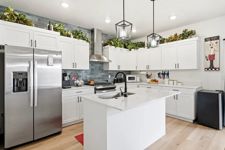 Contemporary kitchen featuring white cabinetry, a large kitchen island with an undermount sink, stainless steel appliances, a modern range hood, and light wood-finish flooring