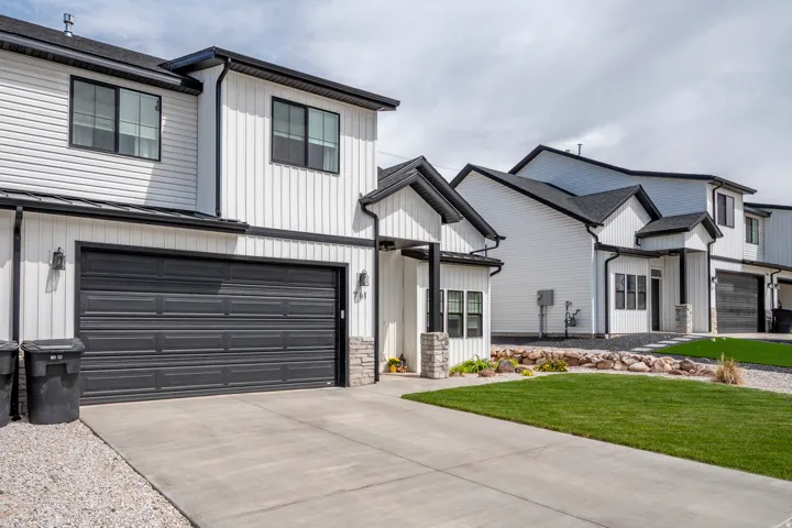 Modern exterior featuring white vertical and horizontal siding, black-framed windows, a black garage door, a paved driveway, and a manicured lawn