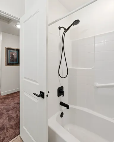 White bathtub with matte black fixtures, integrated shower head, and tile surround