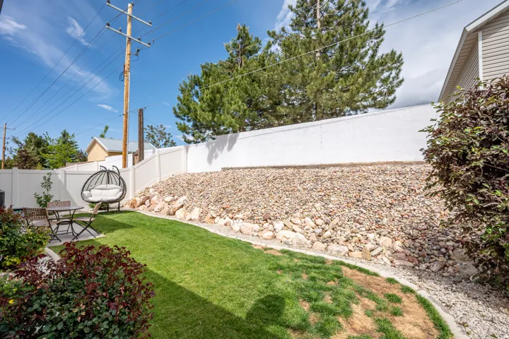 Private backyard featuring a well-maintained lawn, white privacy fencing, and a rock-landscaped incline