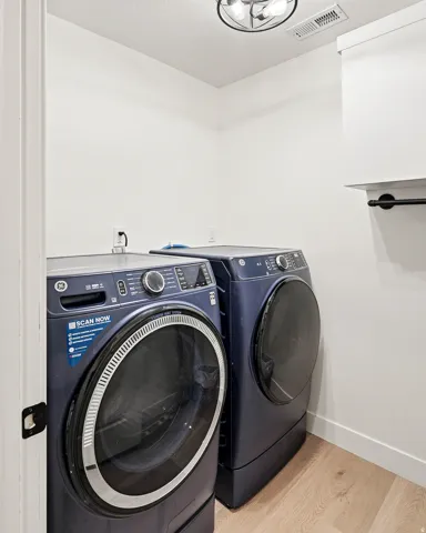 Dedicated laundry space featuring light wood-finish flooring, white walls, and a modern ceiling light fixture