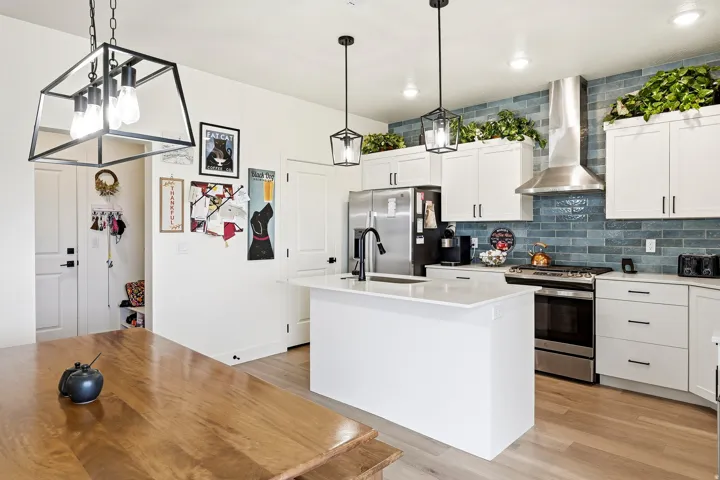 Modern kitchen featuring white cabinetry, light wood-finish flooring, a stainless steel appliance suite, and a blue subway tile backsplash