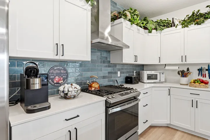 Contemporary kitchen featuring white cabinetry with matte black hardware, a stainless steel range hood, and a blue subway tile backsplash
