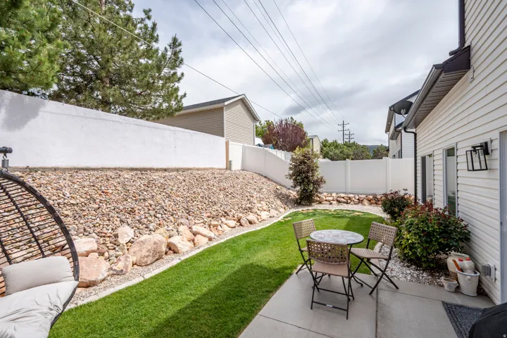 Fenced backyard featuring a concrete patio, a section of manicured lawn, and a rock-landscaped slope