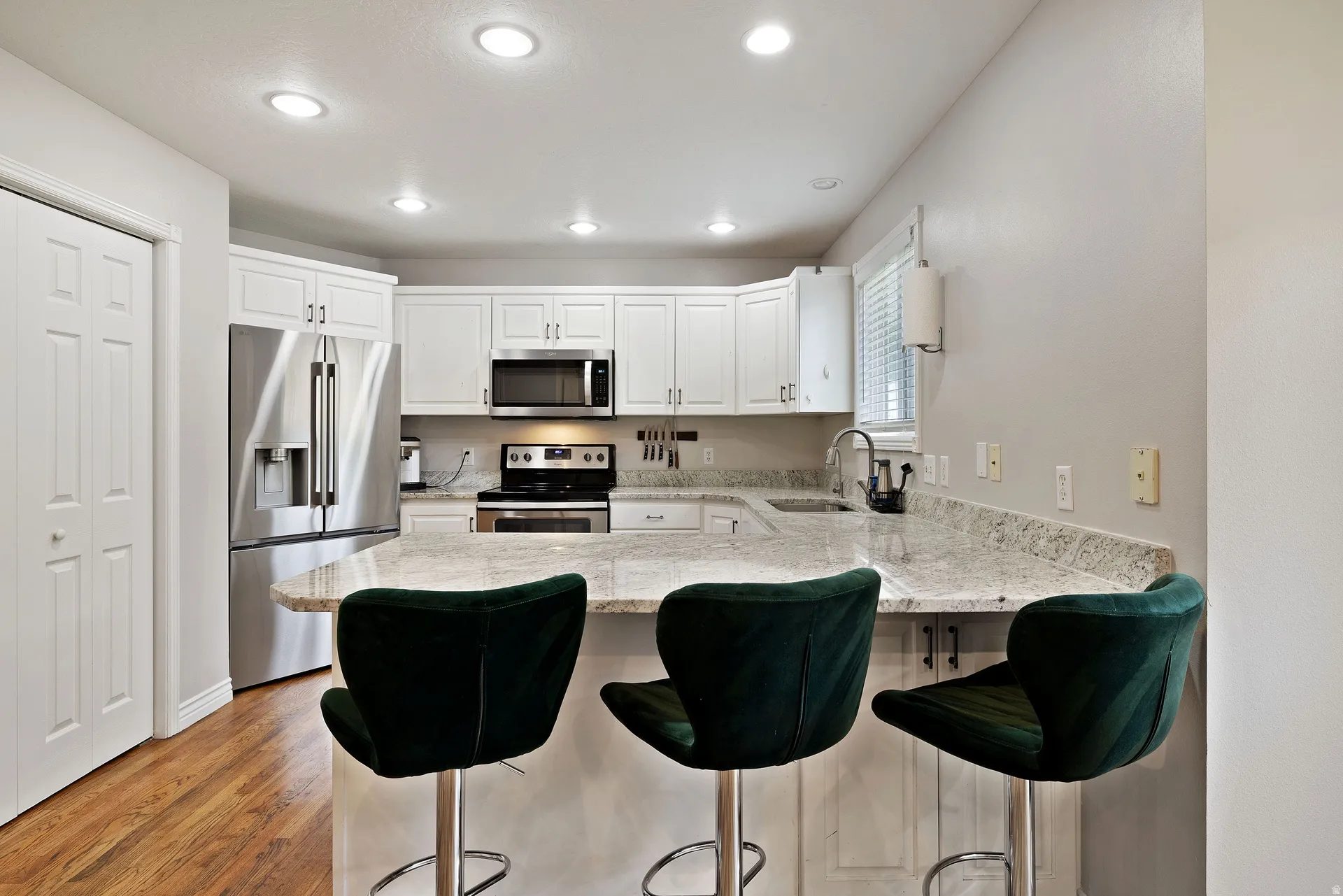 Kitchen featuring wood-finish flooring, white cabinetry, recessed lighting, and a peninsula with a light-toned countertop
