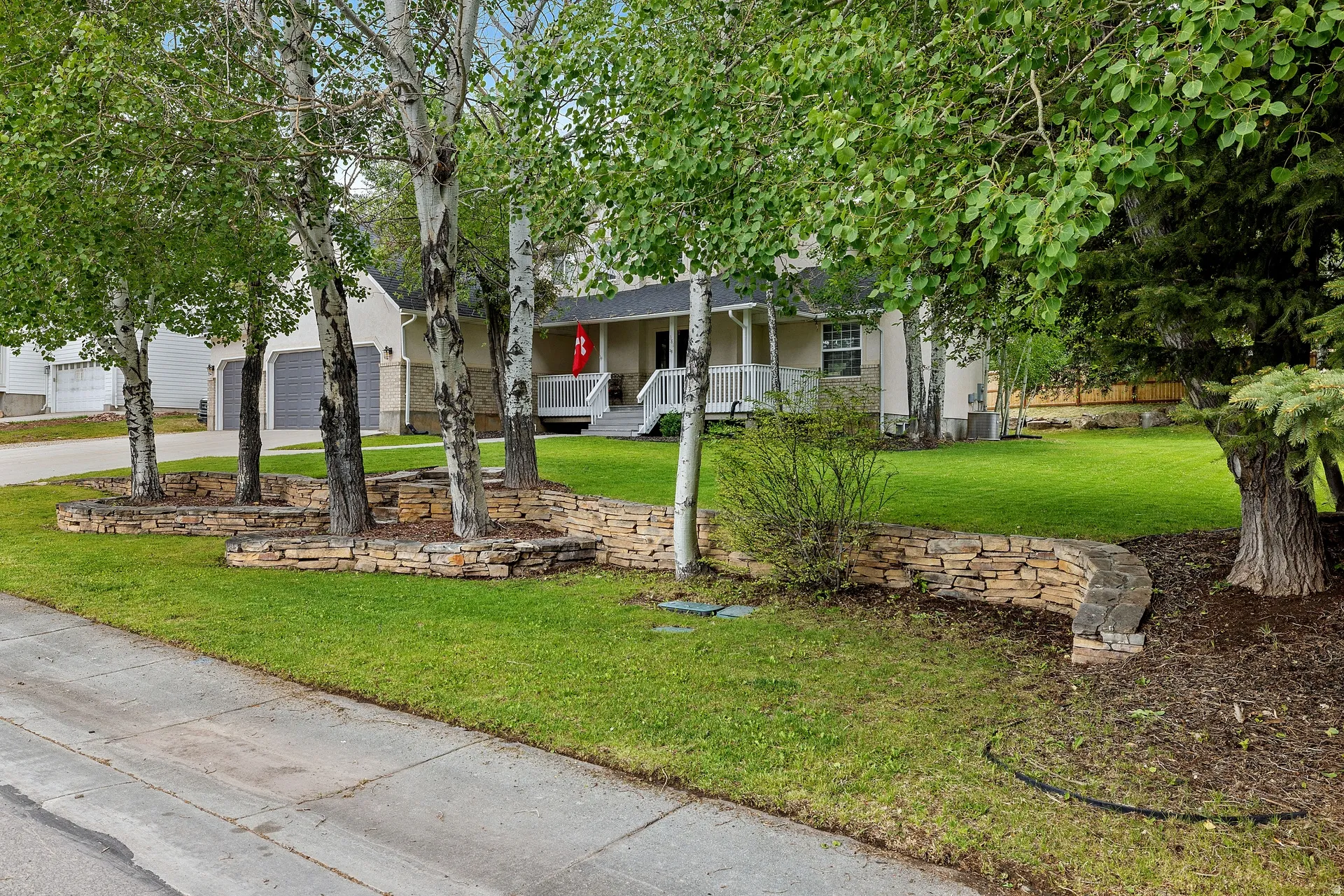 Front yard landscaping featuring multiple mature trees, stone retaining walls, and a manicured lawn