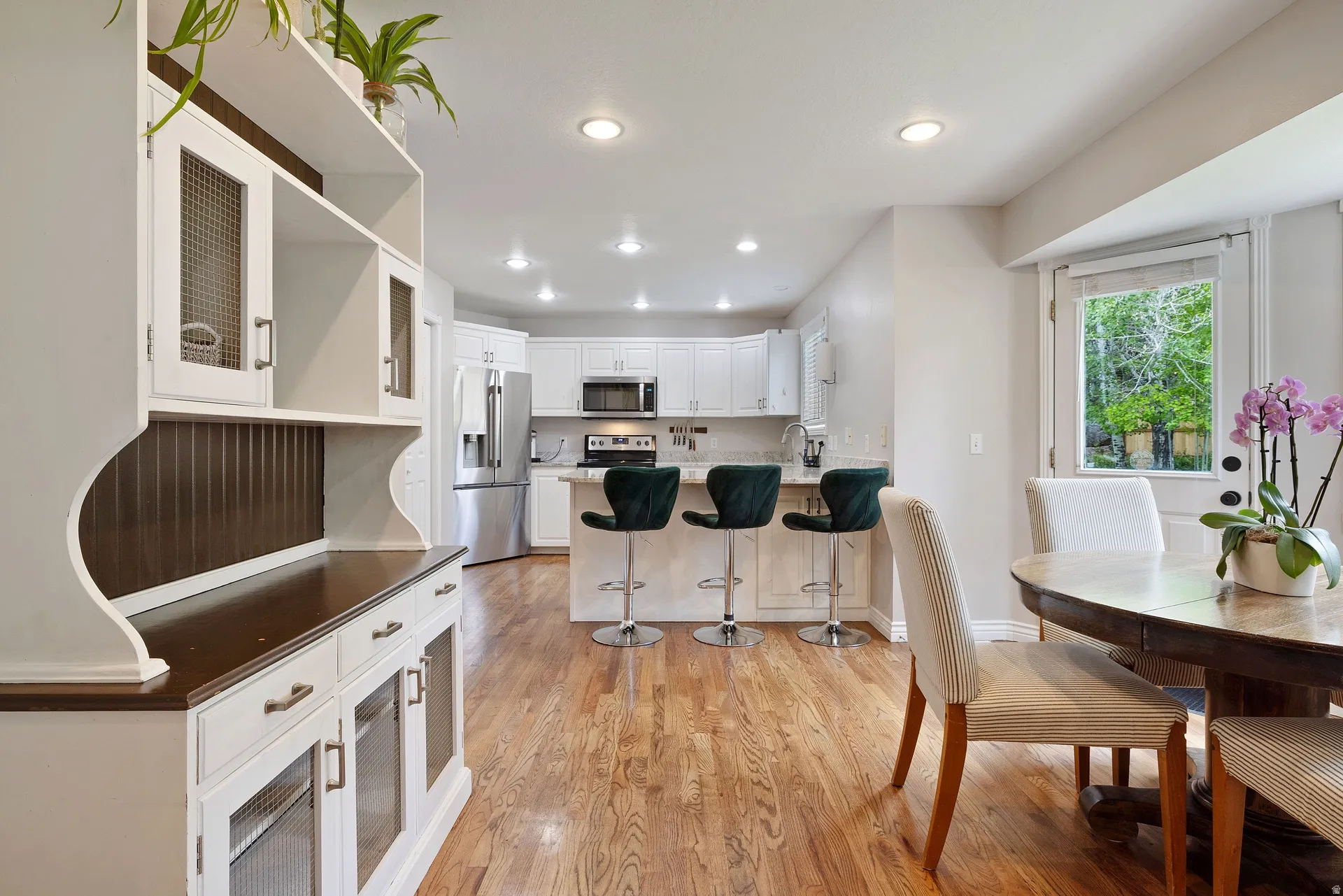 Bright kitchen featuring white cabinetry, stainless steel appliances, a center island with bar seating, wood-finish flooring, and recessed lighting