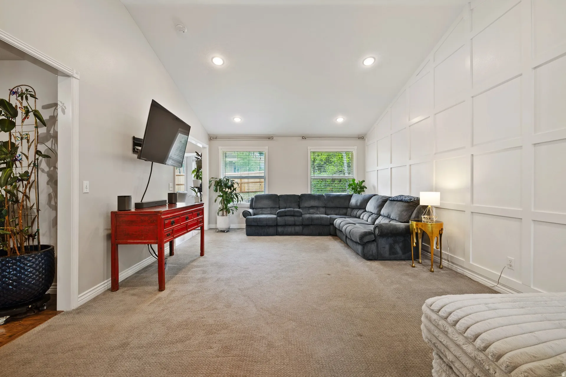 Spacious living area featuring a vaulted ceiling with recessed lighting, a modern accent wall with square paneling, and two windows