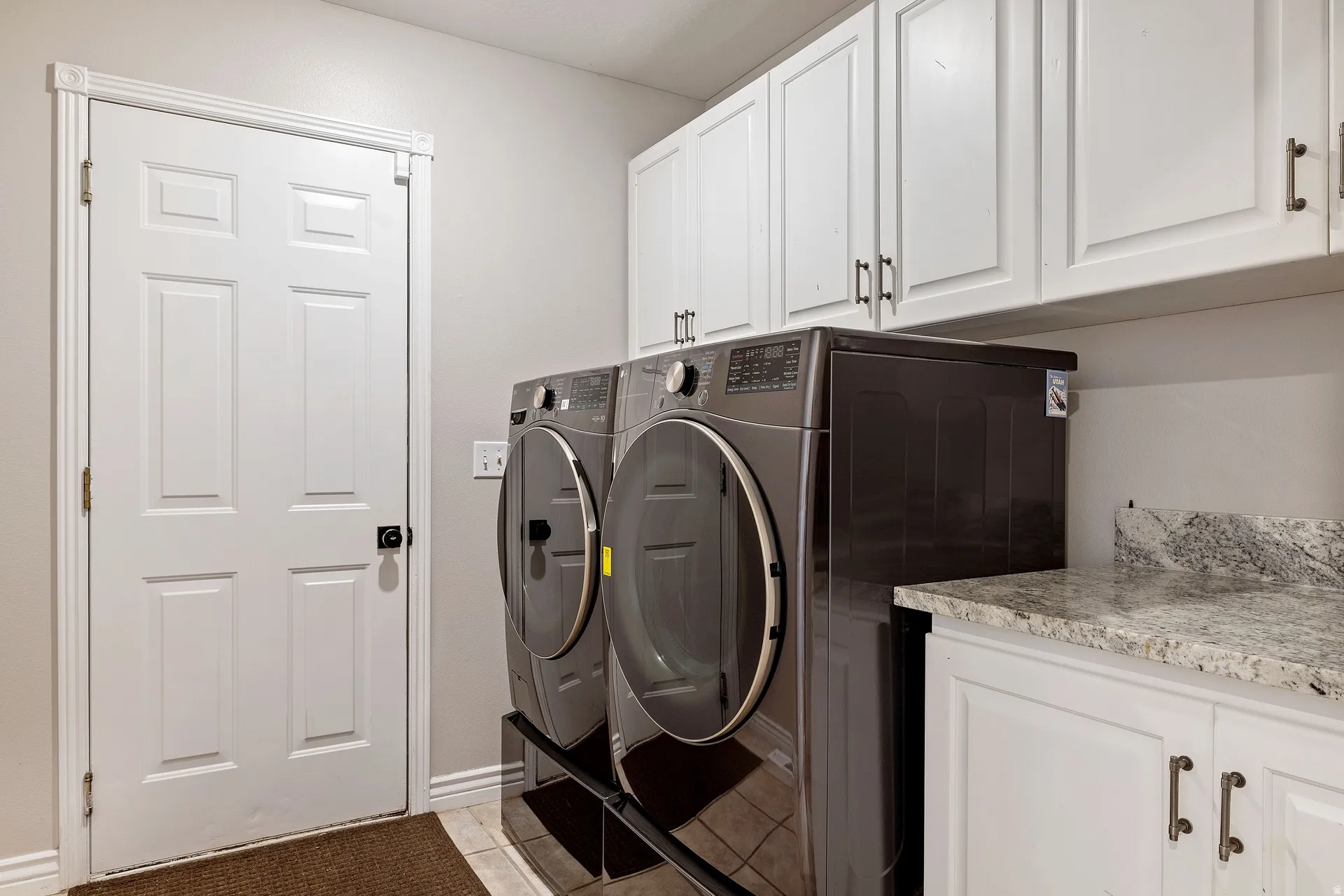 Functional laundry area featuring white shaker-style cabinetry, a light-toned stone-finish countertop, and matching lower cabinets
