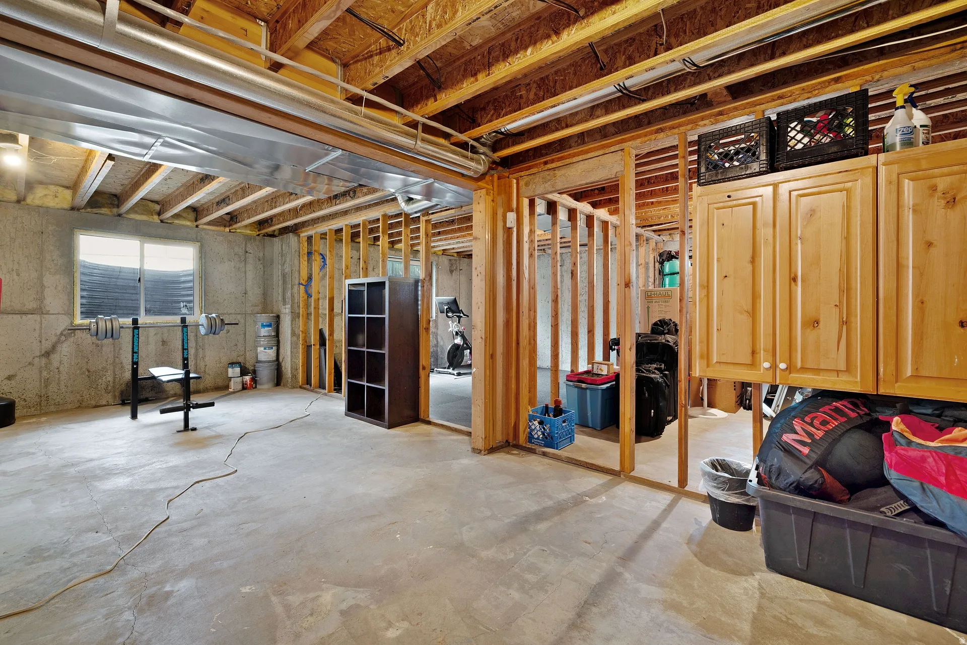Unfinished basement featuring exposed wood joists, concrete flooring, perimeter concrete walls, a single window, and built-in wood cabinetry