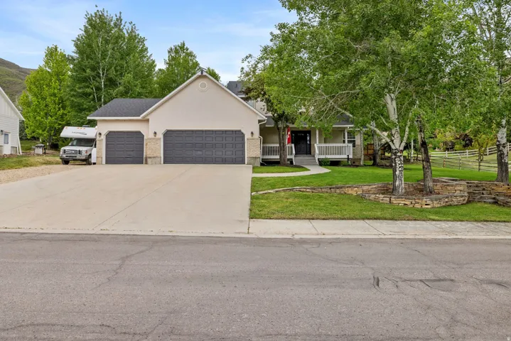 Stucco exterior residence with a two-car garage, a long concrete driveway, and a covered front porch featuring white railing